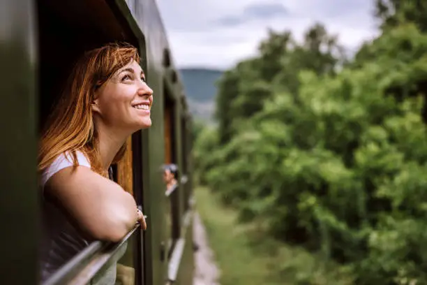 Photo of Young smiling woman standing out of the train window while travelling