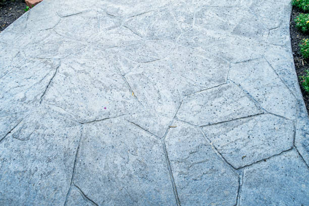 The first raindrops from an imminent rain storm are splattered on a stamped concrete residential home footpath strewn with scattered, random twigs and leaves.