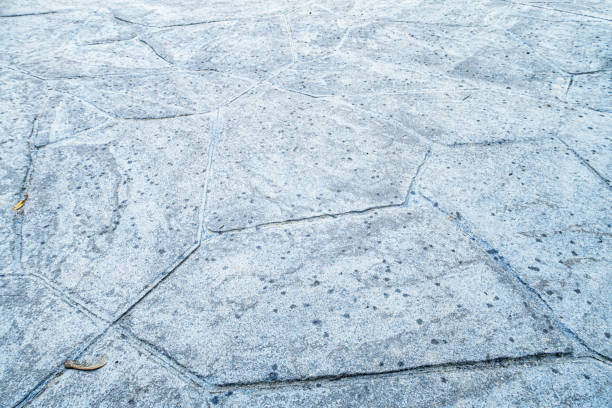 Close-up of the first raindrops from an imminent rain storm splattered on a stamped concrete residential home footpath strewn with scattered, random twigs and leaves.