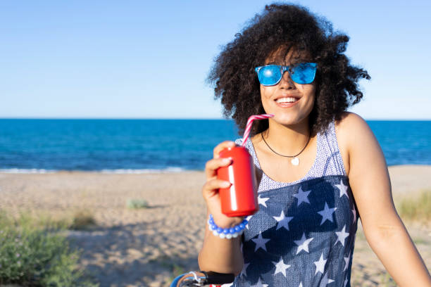 istock Carefree african woman drinking red can on beach 1168489503