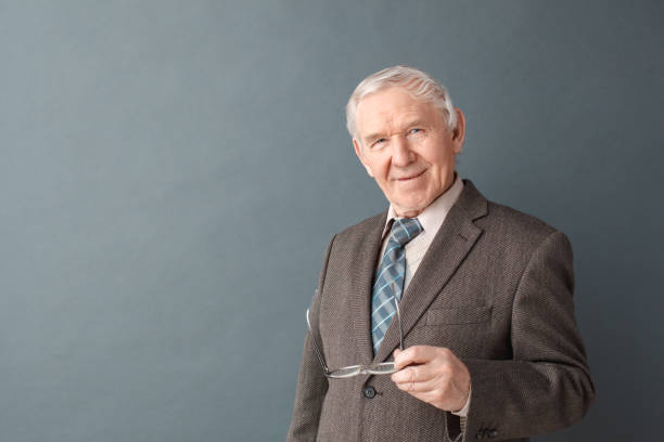 istock Senior man studio standing isolated on gray holding glasses looking camera joyful 1168489602