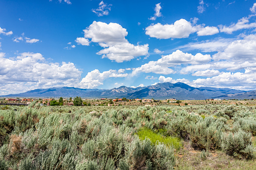 View of Taos Sangre de Cristo mountains view from Ranchos de Taos valley and green landscape in summer with clouds