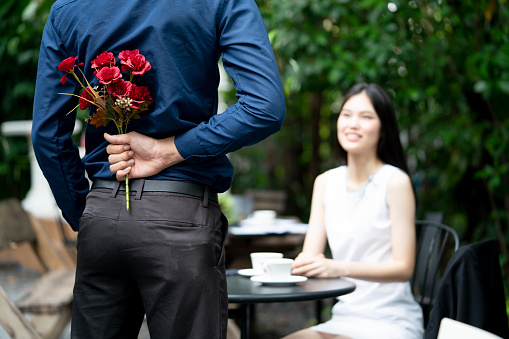 A man is proposing marriage to a smiling woman with a lovely flower bouquet in a beautiful garden, lover and couple concept, surprising proposal