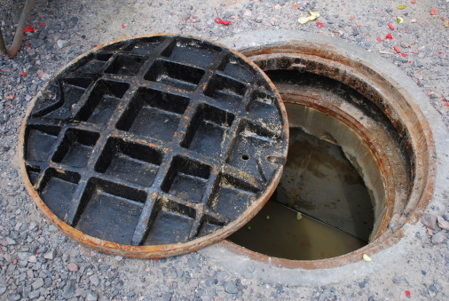 Partially open manhole on a street with water/sewage visible below