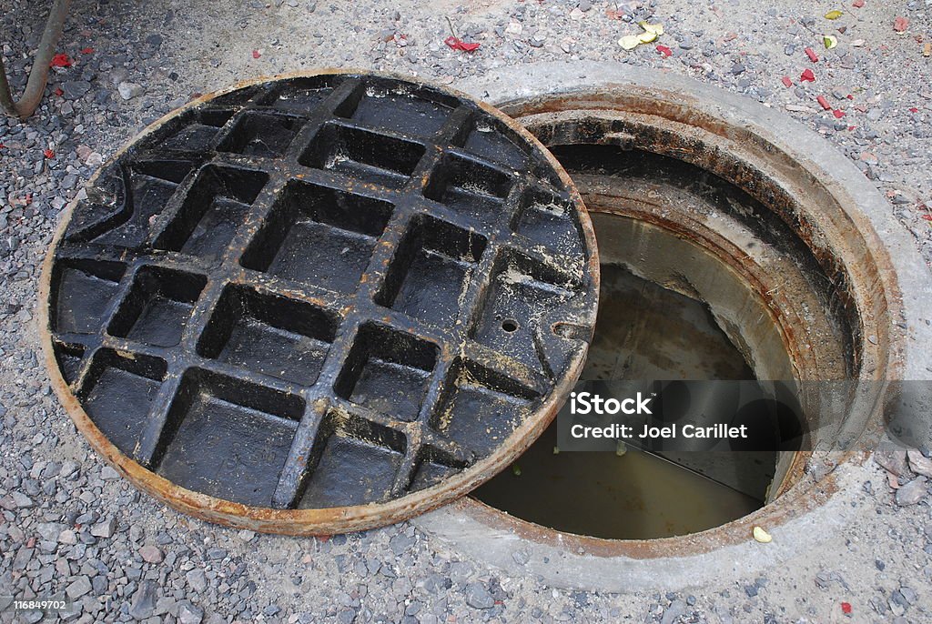 Open Manhole Partially open manhole on a street with water/sewage visible below Sewage Stock Photo