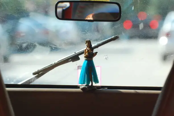 A small statue of a girl in a hula skirt playing the ukulele on the dashboard of a car.