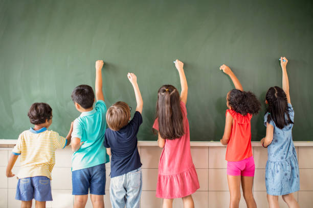 Groupe multiethnique d'enfants d'école dessinant sur le tableau - Photo