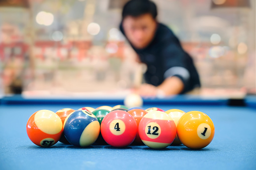 The colorful billiard or pool balls for snooker game are on blue billiard table for starting the match with blur image of player.