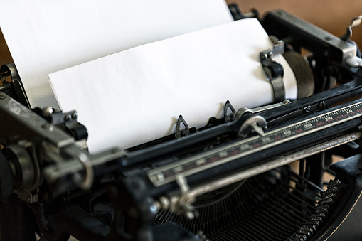 Close-up of an old-fashioned manual typewriter with selective focus on the blank piece of white typing paper rolled into the manual paper roller - all ready for the inky keys to start hammering away.