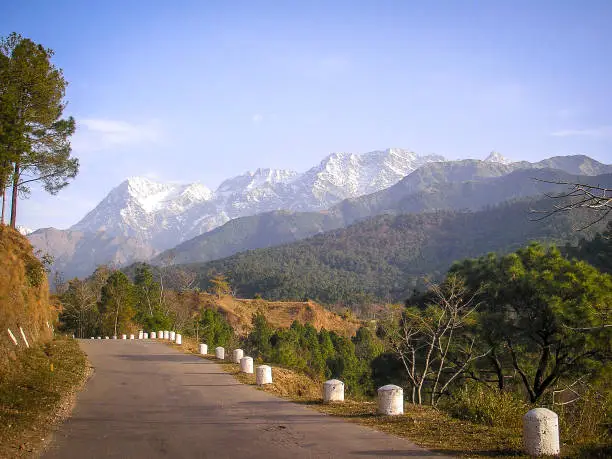 Concrete bitumen mountain road with white pillars against a scenic background of himalayan foothills and snow capped mountains
