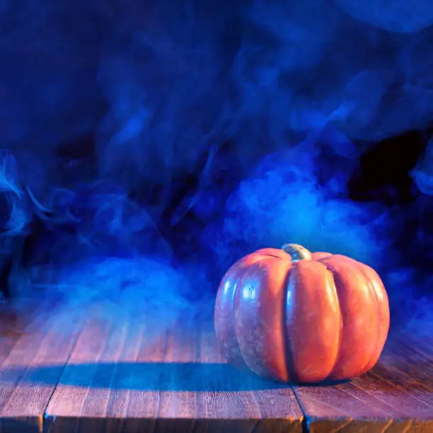 Photo of Halloween concept - Orange pumpkin lantern on a dark wooden table with double colored smoke around the background, trick or treat.