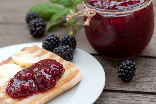 Asian mother helps her young son spread berry jam on toast while sharing a breakfast moment in home kitchen.