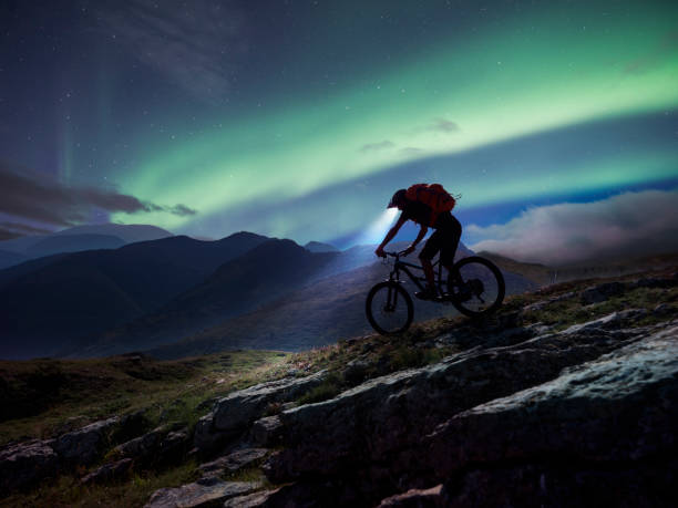 ciclista de montaña montando en montaña bajo aurora polaris. - mountain biking extreme sports cycling bicycle fotografías e imágenes de stock