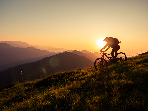 Mountain biker riding downhill in mountain at sunset, living adventure.