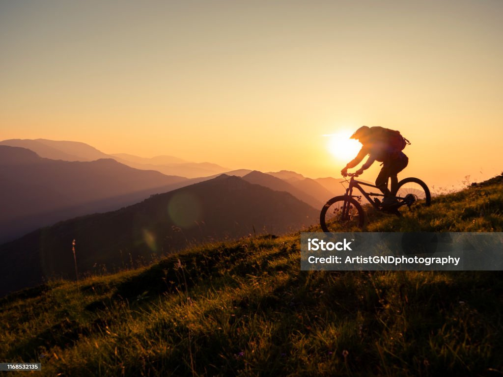 Mountain biker riding downhill in mountain. Mountain biker riding downhill in mountain at sunset, living adventure. Cycling Stock Photo