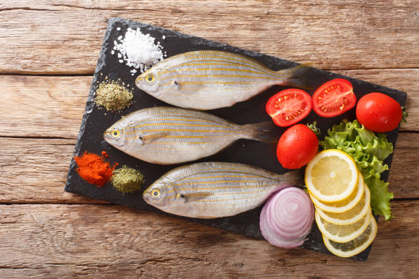 Preparation for cooking Sarpa salpa fish with lemon, vegetables and spices close-up on a slate board. horizontal top view Preparation for cooking Sarpa salpa fish with lemon, vegetables and spices close-up on a slate board on the table. horizontal top view from above salpa stock pictures, royalty-free photos & images