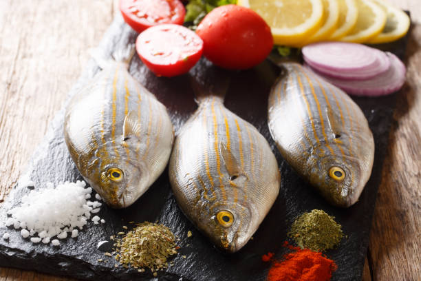 Fresh raw raw sarpa salpa fish with lemon, vegetables and spices closeup on a slate board. Horizontal Fresh raw raw sarpa salpa fish with lemon, vegetables and spices closeup on a slate board on a table. Horizontal salpa stock pictures, royalty-free photos & images