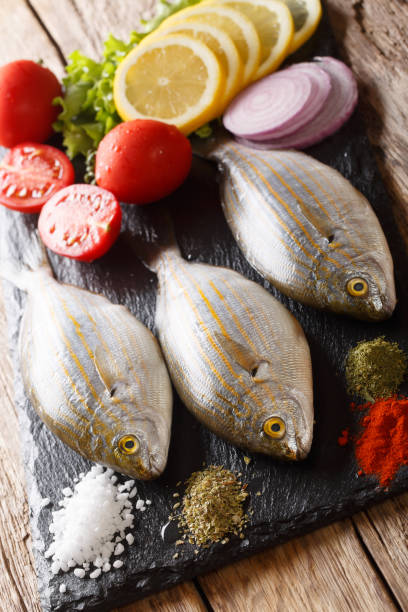 Mediterranean raw sarpa salpa fish with lemon, vegetables and spices close up served on a slate board. vertical Mediterranean raw sarpa salpa fish with lemon, vegetables and spices close up served on a slate board on a table. vertical salpa stock pictures, royalty-free photos & images