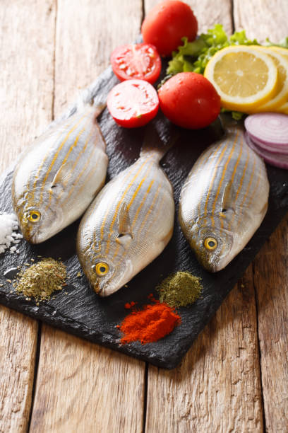 Preparation for cooking Sarpa salpa fish with lemon, vegetables and spices close-up on a slate board. vertical Preparation for cooking Sarpa salpa fish with lemon, vegetables and spices close-up on a slate board on the table. vertical salpa stock pictures, royalty-free photos & images