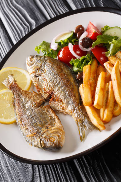 Fried Mediterranean Sarpa salpa fish served with fresh salad and french fries close-up on a plate. vertical Fried Mediterranean Sarpa salpa fish served with fresh salad and french fries close-up on a plate on the table. vertical salpa stock pictures, royalty-free photos & images