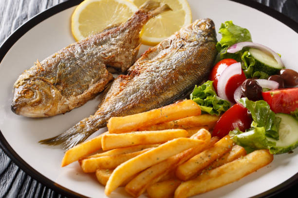 Portion of fried Salema porgy fish with lemon and fresh vegetable salad close-up on a plate. horizontal Portion of fried Salema porgy fish with lemon and fresh vegetable salad close-up on a plate on the table. horizontal salpa stock pictures, royalty-free photos & images