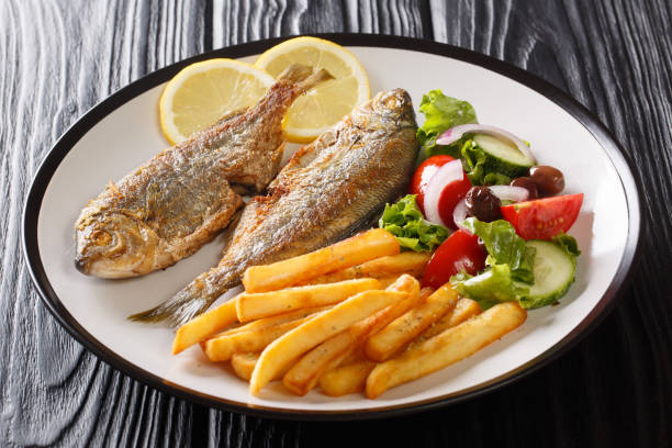 Adriatic fried Sarpa salpa fish with lemon served with fresh vegetable salad and french fries close-up on a plate. horizontal Adriatic fried Sarpa salpa fish with lemon served with fresh vegetable salad and french fries close-up on a plate on the table. horizontal salpa stock pictures, royalty-free photos & images