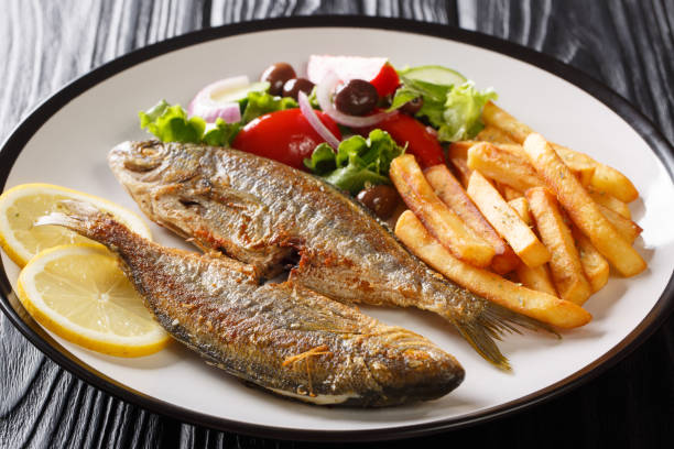 Mediterranean cuisine Fried Sarpa fish with fresh vegetable salad, lemon and french fries close-up on a plate. horizontal Mediterranean cuisine Fried Sarpa fish with fresh vegetable salad, lemon and french fries close-up on a plate on the table. horizontal salpa stock pictures, royalty-free photos & images