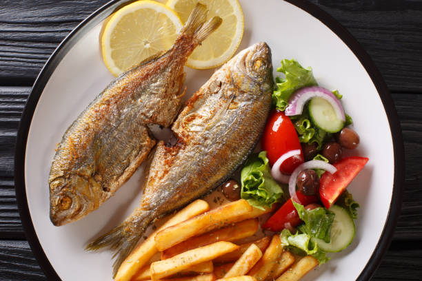 Fried Salema porgy fish with a side dish of fresh salad and french fries close-up on a plate. horizontal top view Fried Salema porgy fish with a side dish of fresh salad and french fries close-up on a plate on the table. horizontal top view from above salpa stock pictures, royalty-free photos & images