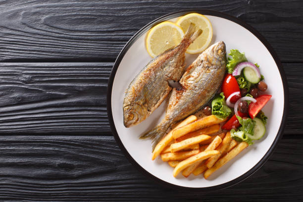 Traditional fried Sarpa salpa fish with lemon and side dish of fresh vegetable salad. french fries close-up on a plate. horizontal top view Traditional fried Sarpa salpa fish with lemon and side dish of fresh vegetable salad and french fries close-up on a plate on the table. horizontal top view from above salpa stock pictures, royalty-free photos & images
