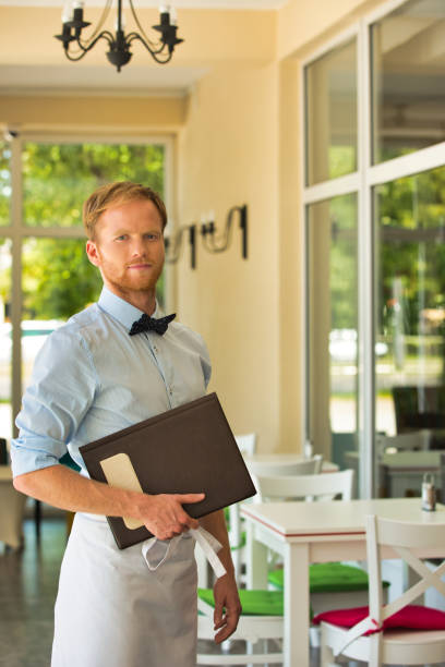 istock Portrait of confident young waiter holding menu while standing at restaurant 1168538846