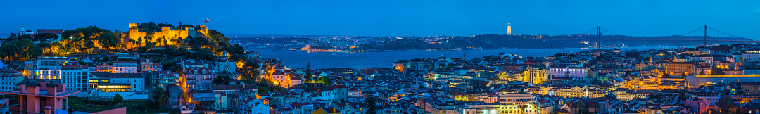Panoramic illuminated night view over the rooftops of Lisbon from Sao Jorge to the iconic towers of the 25 de Abril bridge over the Tagus in the heart of Lisbon, Portugal’s vibrant capital city.