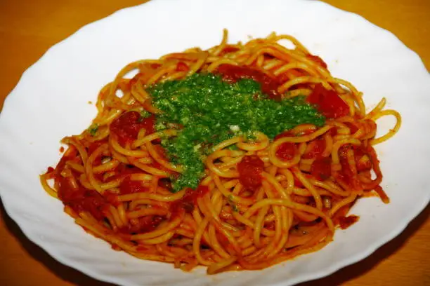 close-up of a plate with pasta, tomatosauce, basil and other herbs