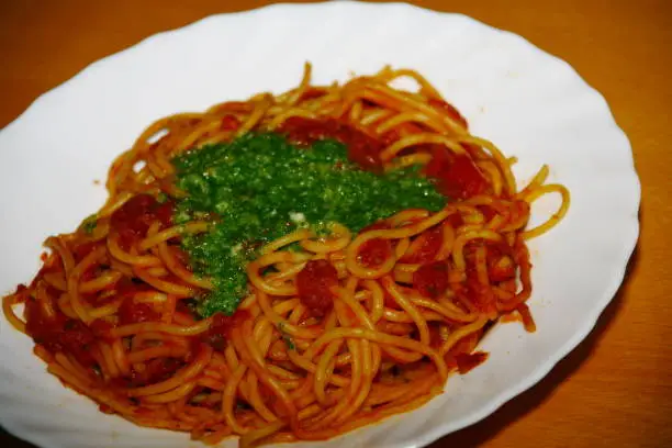 close-up of a plate with pasta, tomatosauce, basil and other herbs