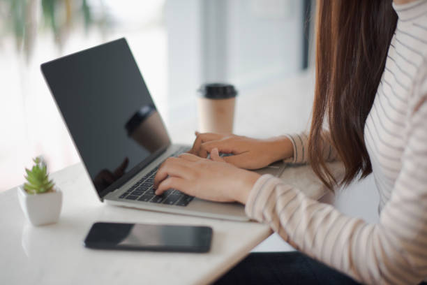 istock Closed up and focus on hand of young woman using a notebook laptop which put on white table and have smartphone and cup of coffee in near at cafe coffee shop. co working space concept. 1168547289