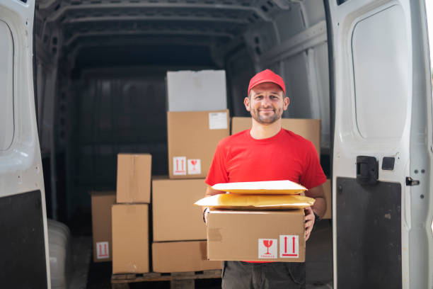 Portrait of delivery man in front of delivery van. Delivery man in red uniform in front of delivery van, holding packages and looking at camera, he  loading packages in van. delivery person stock pictures, royalty-free photos & images