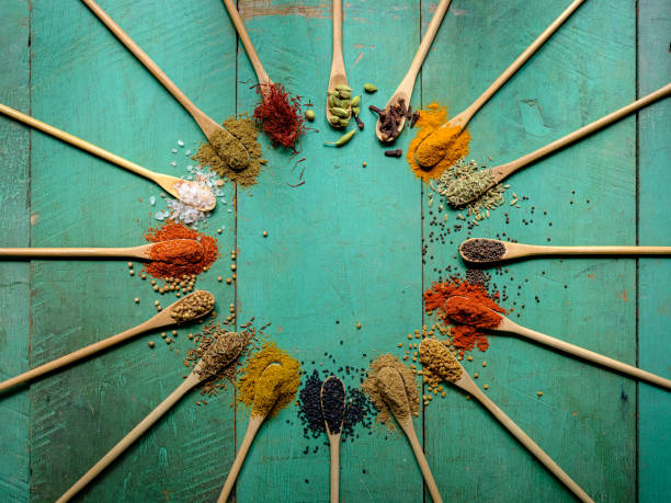 variedade de especiarias indianas coloridas, secadas, vibrantes do alimento em colheres de madeira em um fundo de madeira colorido turquesa velho, com iluminação atmosférica. - cardamom spice herb food - fotografias e filmes do acervo