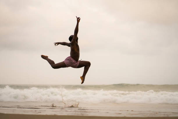 istock dramatic contemporary dance choreographer doing ballet beach workout . young attractive and athletic afro black American man dancing on sunrise jumping doing performance rehearsal 1168550053