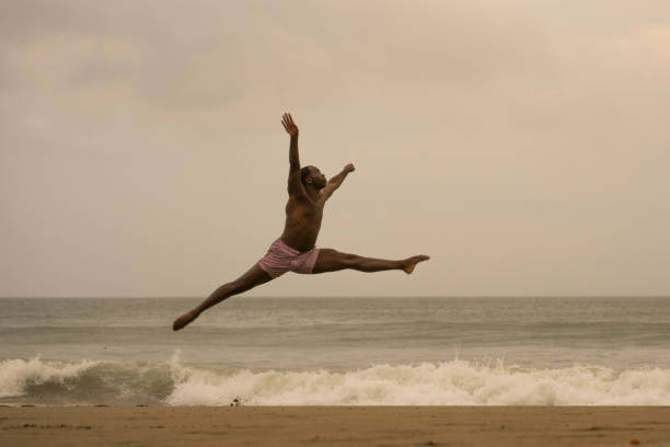 istock dramatic contemporary dance choreographer doing ballet beach workout . young attractive and athletic afro black American man dancing on sunrise jumping doing performance rehearsal 1168550146