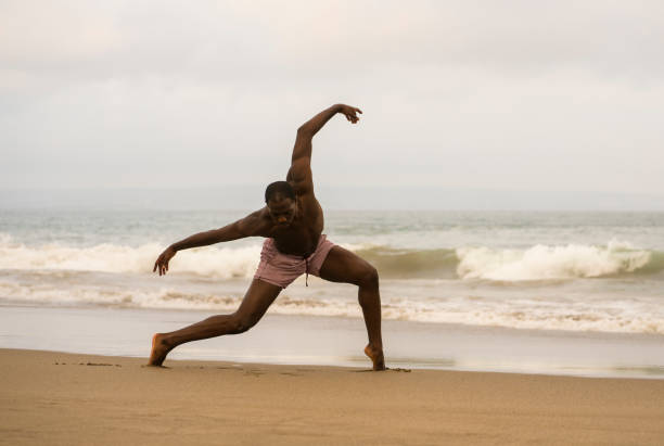 istock dramatic contemporary dance choreographer doing ballet beach workout . young attractive and athletic afro black American man dancing on sunrise doing performance rehearsal 1168550147
