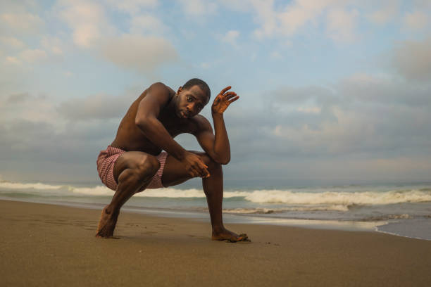 dramatic contemporary dance choreographer doing ballet beach workout . young attractive and athletic afro black American man dancing on sunrise doing performance rehearsal dramatic contemporary dance choreographer doing ballet beach workout . young attractive and athletic afro black American man dancing on sunrise doing performance rehearsal contemporary dance stock pictures, royalty-free photos & images