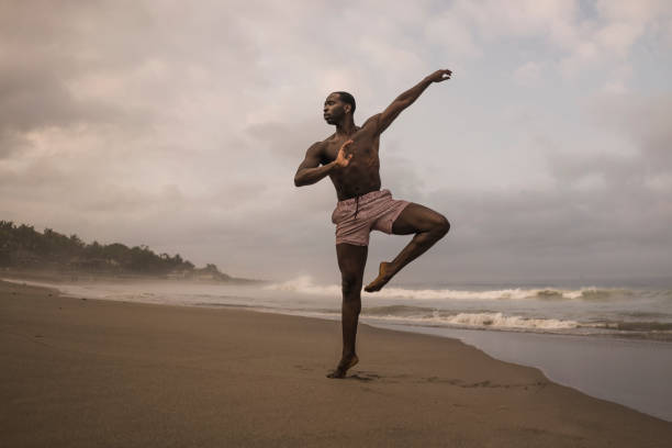 istock dramatic contemporary dance choreographer doing ballet beach workout . young attractive and athletic afro black American man dancing on sunrise doing performance rehearsal 1168551053