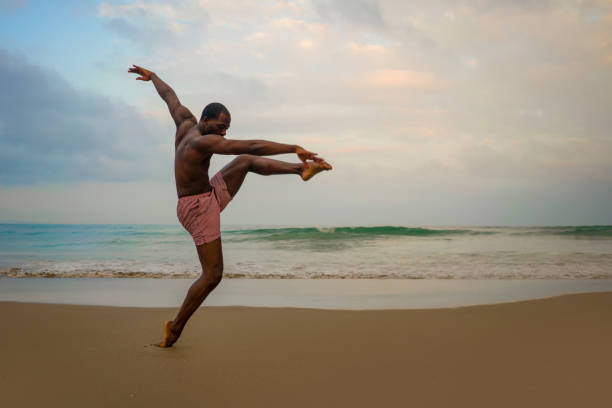 istock dramatic contemporary dance choreographer doing ballet beach workout . young attractive and athletic afro black American man dancing on sunrise doing performance rehearsal 1168551134