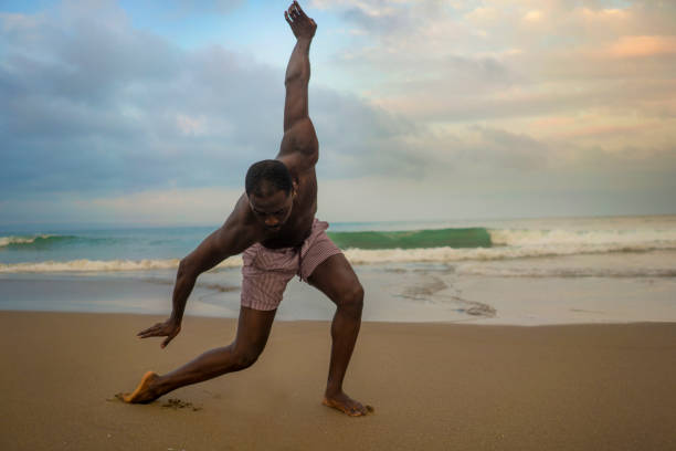 istock dramatic contemporary dance choreographer doing ballet beach workout . young attractive and athletic afro black American man dancing on sunrise doing performance rehearsal 1168551274