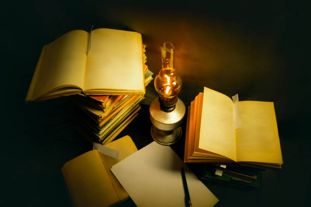 Old open books are lying on the table, lit by a kerosene lamp.