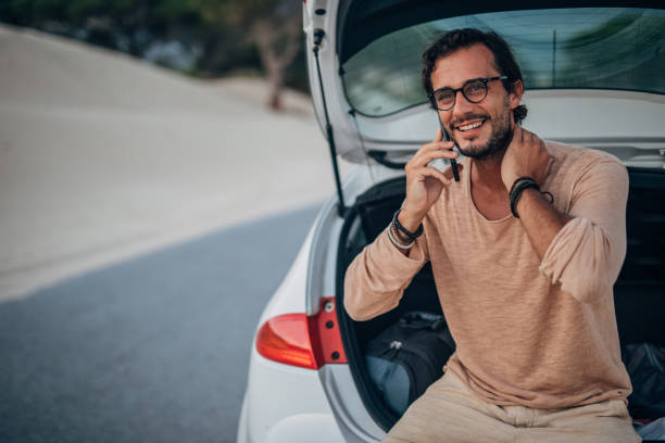 istock Guy sitting on car trunk and talking on mobile 1168558728