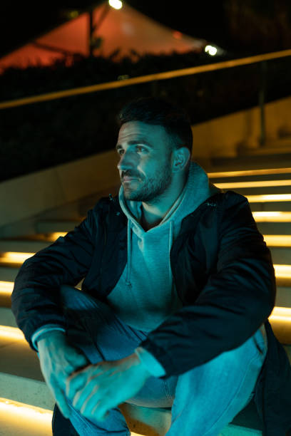 Casual man waiting outdoors at night on an illuminated street staircase stock photo