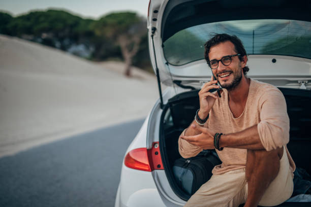 istock Man sitting on car trunk and talking on mobile 1168558742