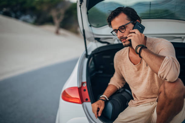 istock Man sitting on car trunk and talking on phone 1168558760