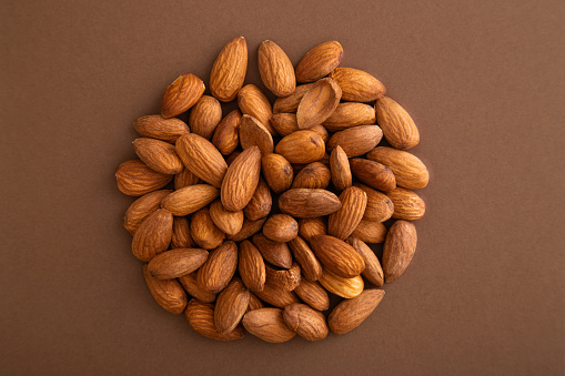Almonds heap in a circle form on a brown background viewed from above. Nuts creative layout. Top view
