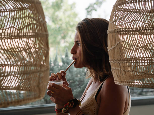 chica caucásica está comiendo entre dos lámparas de mimbre y frente a la ventana. - women spoon tasting elegance fotografías e imágenes de stock